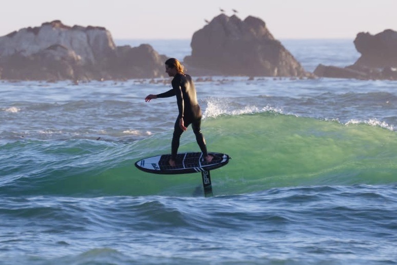 Surfer gliding on a wave using a foil board near rocky shore in Cape Town, Molo Africa Kite School
